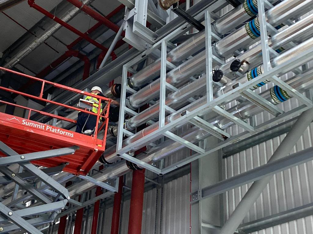Operative installing insulated pipework on a steel support frame from an elevated platform